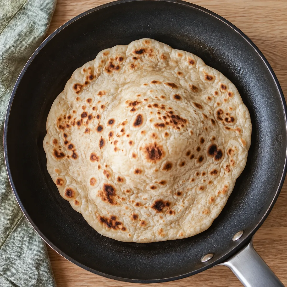 Een platbrood dat in een droge pan opbolt met bruine vlekken